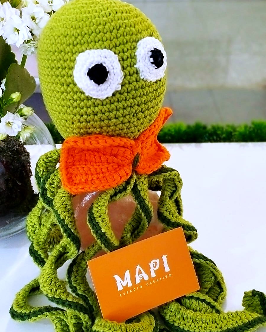 Pulpito verde de crochet con panuelo naranja sosteniendo tarjeta MAPI