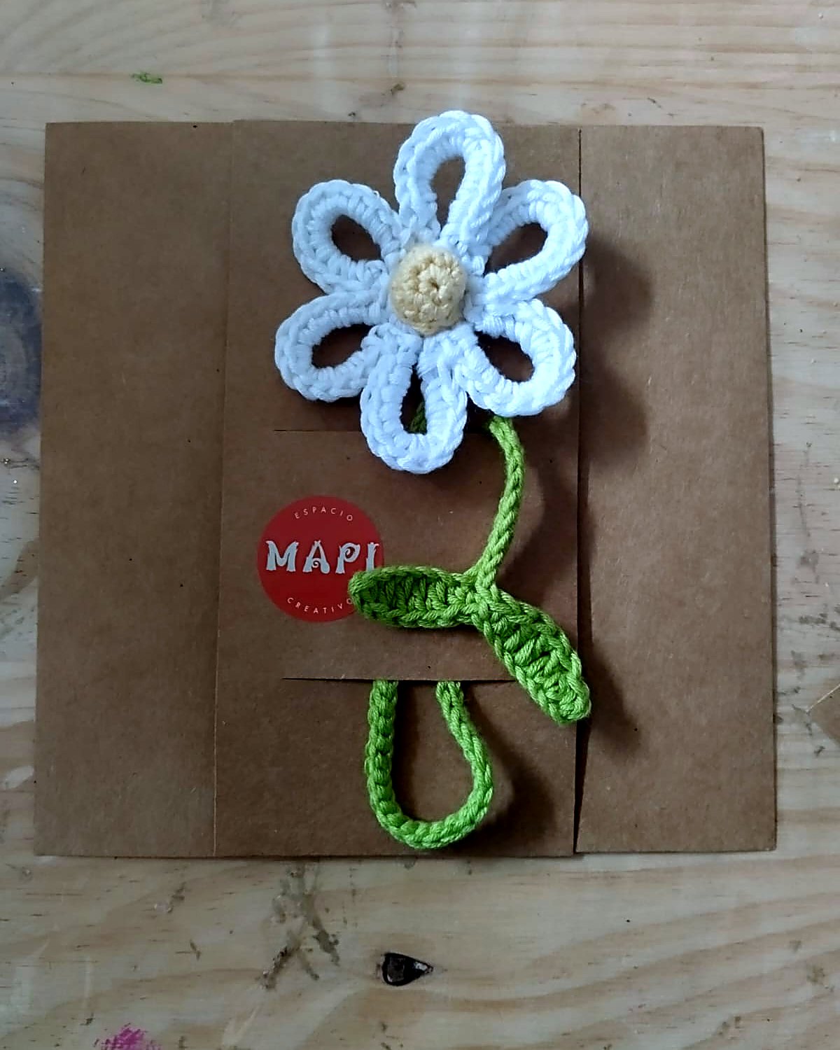 Marcapaginas de flor de crochet azul con pegatina MAPI sobre libreta kraft