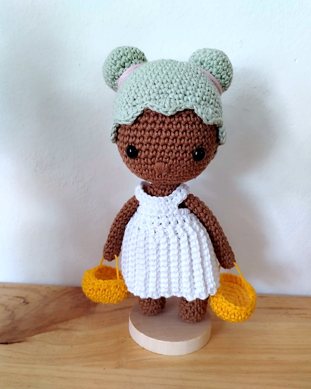 Muneca amigurumi de piel morena con gorro de osito y vestido blanco