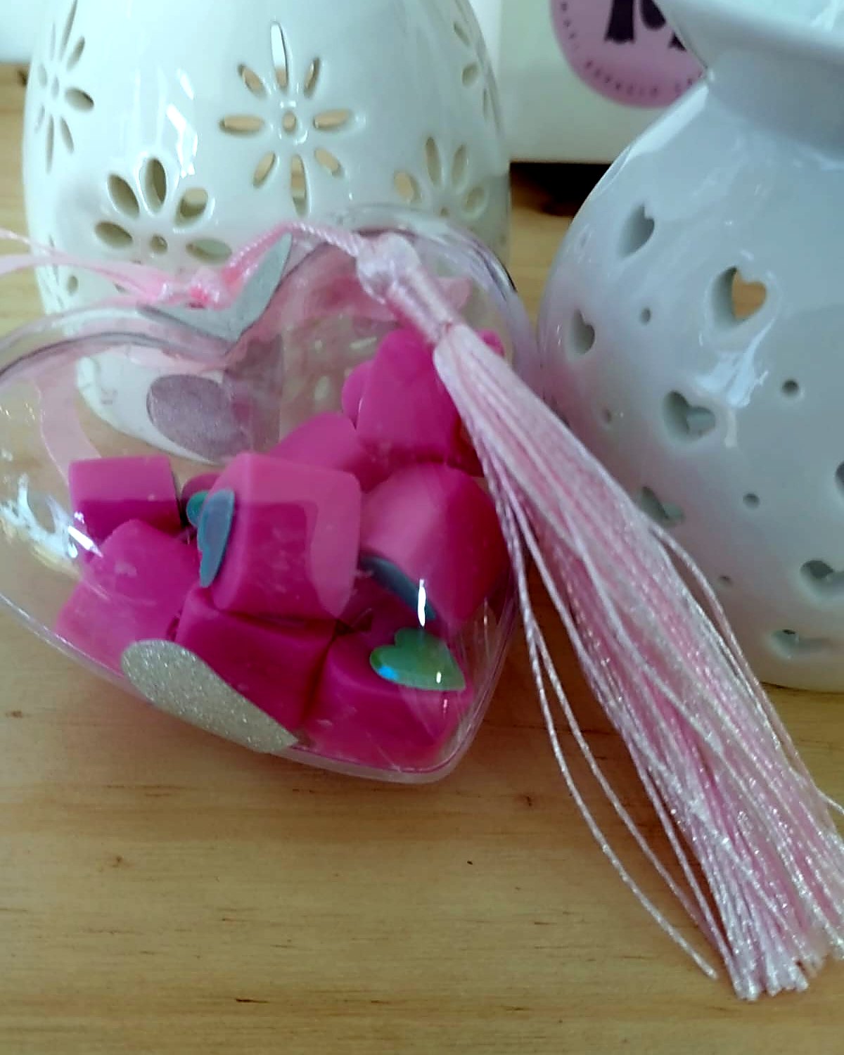 Bolsa transparente con tabletas de cera rosa y borla, junto a quemadores