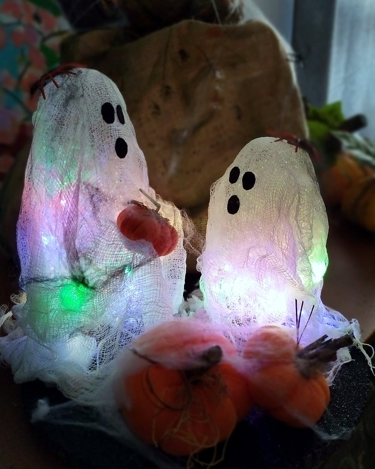 Dos fantasmas iluminados con luces de colores y calabazas