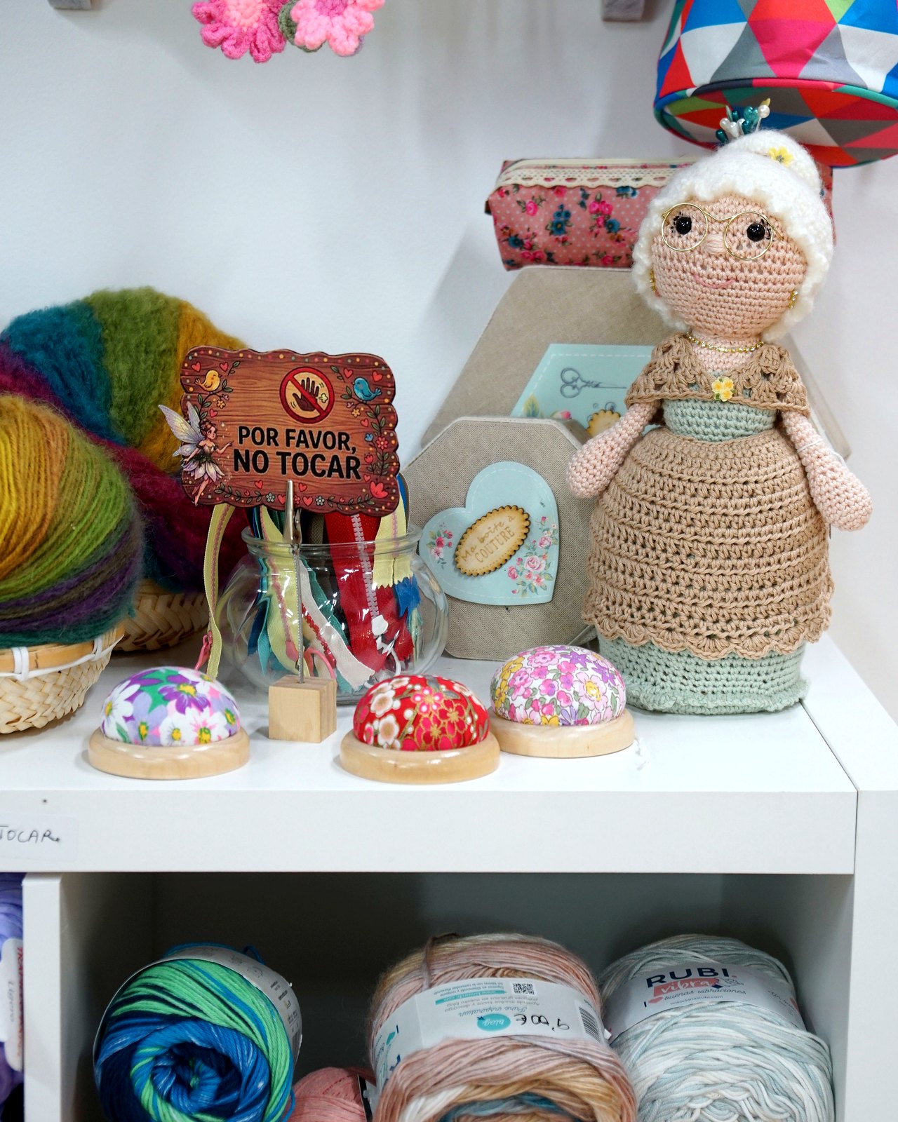 Muneca amigurumi sobre expositor con lanas y agujas
