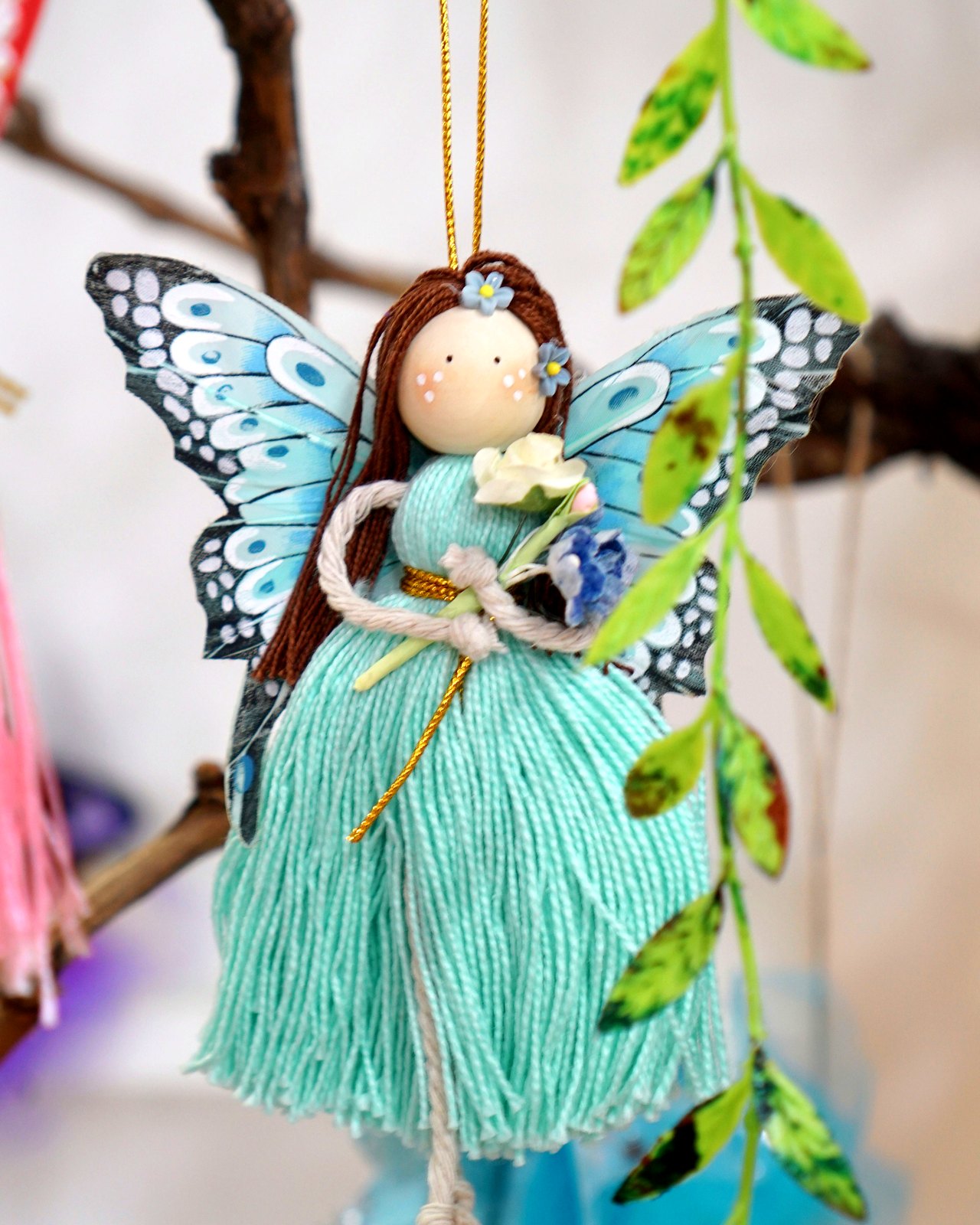 Hada colgante turquesa con alas de mariposa y falda de flecos, sobre rama